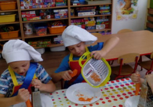 Dwóch chłopców podczas ścierania marchewek na tarkach.